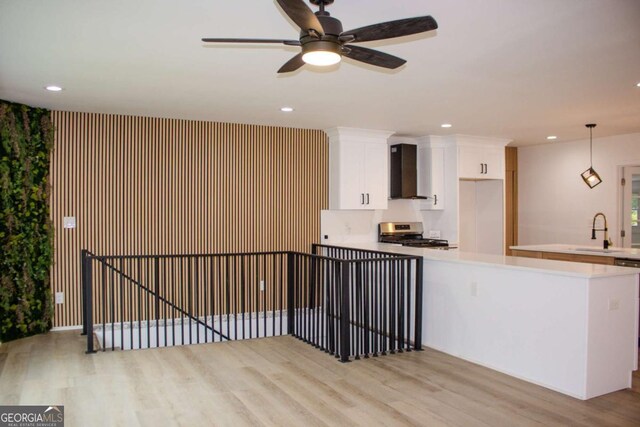 kitchen with wall chimney exhaust hood, light wood-type flooring, stainless steel range with gas cooktop, white cabinetry, and a sink