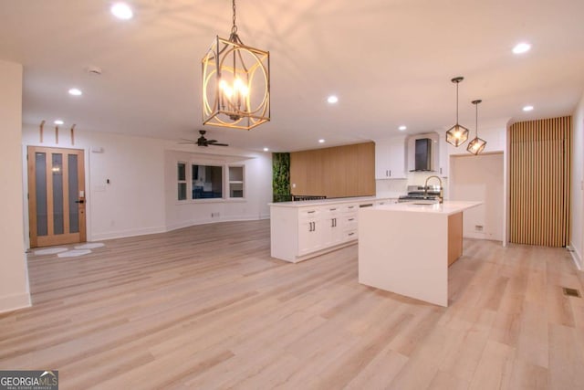 kitchen featuring light wood-style floors, recessed lighting, wall chimney range hood, and an island with sink