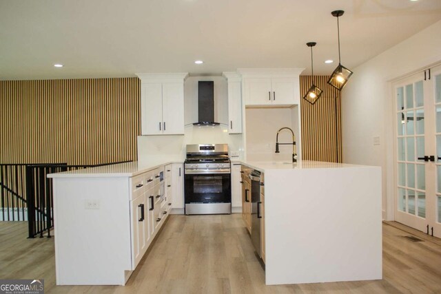 kitchen featuring light wood finished floors, stainless steel appliances, light countertops, wall chimney range hood, and white cabinetry