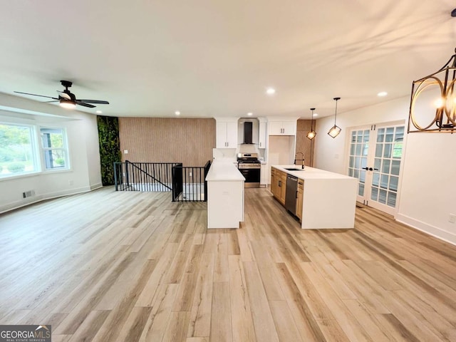 kitchen with a center island with sink, appliances with stainless steel finishes, a sink, wall chimney range hood, and light wood-type flooring