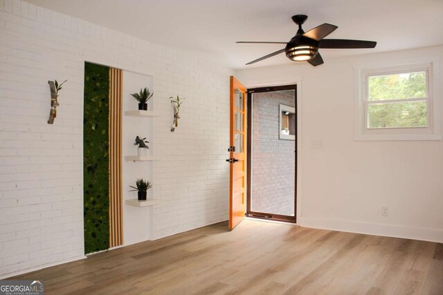 empty room featuring a ceiling fan, brick wall, baseboards, and wood finished floors