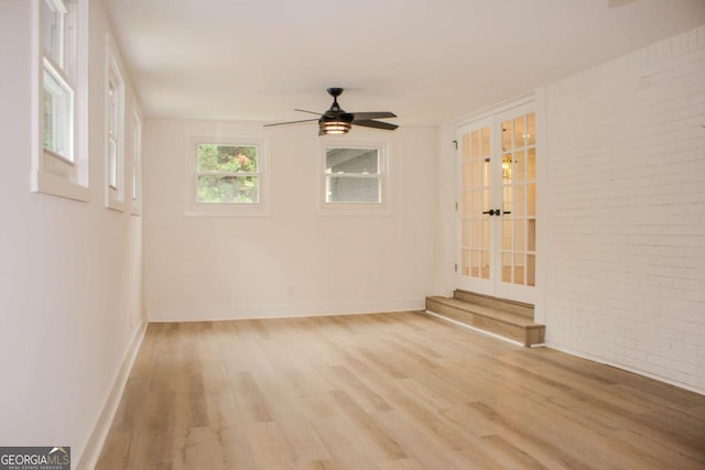 spare room featuring brick wall, light wood-style flooring, baseboards, and a ceiling fan