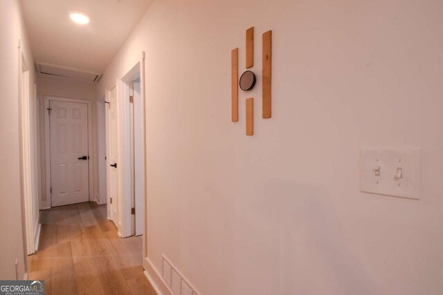 corridor with light wood finished floors, attic access, and visible vents