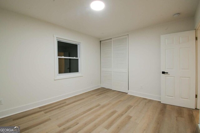 unfurnished bedroom featuring light wood finished floors, a closet, and baseboards