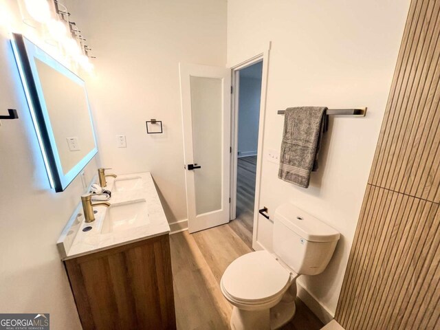 bathroom with toilet, double vanity, a sink, and wood finished floors