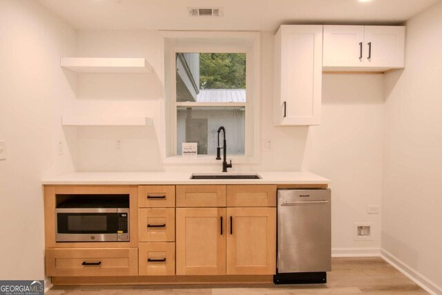 kitchen with open shelves, light countertops, stainless steel microwave, visible vents, and a sink