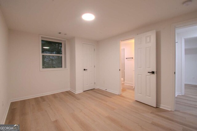 unfurnished bedroom featuring light wood-style flooring, baseboards, and ensuite bathroom