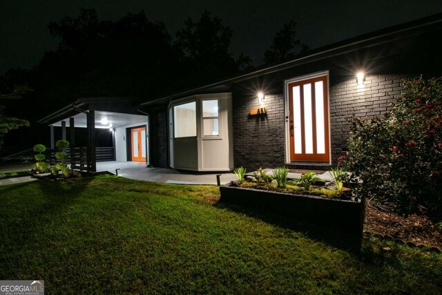 back of house at night with brick siding and a lawn