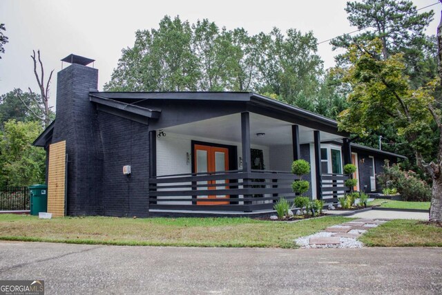 view of front of home with covered porch, a chimney, french doors, and brick siding