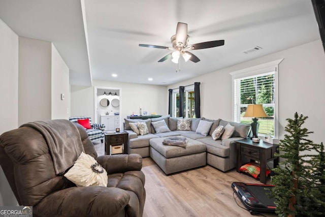 living room with light wood finished floors, visible vents, and a ceiling fan