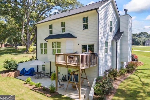 rear view of property featuring a lawn, a chimney, a wooden deck, and a patio