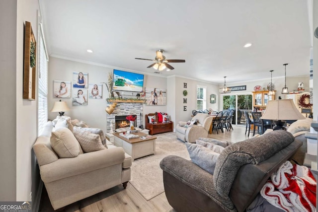 living area with light wood-style floors, a fireplace, a ceiling fan, and crown molding