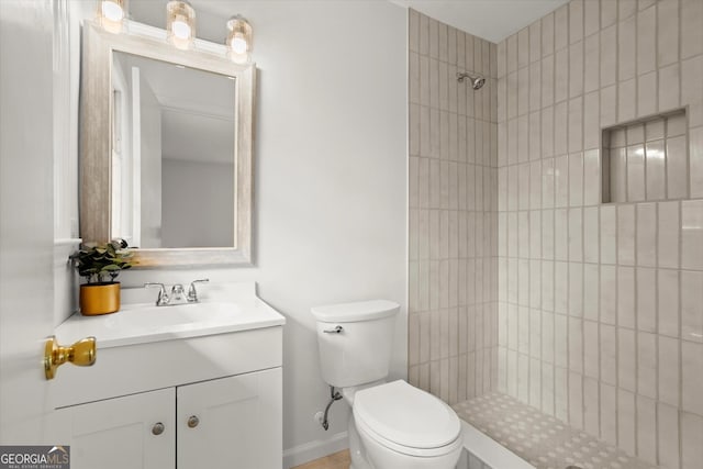 bathroom with baseboards, a tile shower, vanity, and toilet