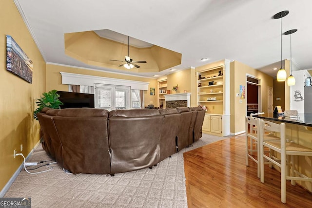 living room with a fireplace, a ceiling fan, baseboards, a tray ceiling, and crown molding