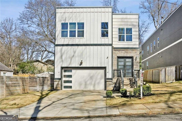 contemporary house with stone siding, board and batten siding, concrete driveway, and fence