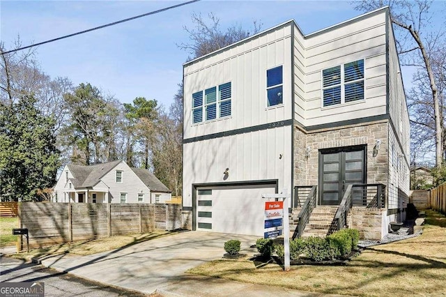 modern home with fence, an attached garage, concrete driveway, stone siding, and board and batten siding