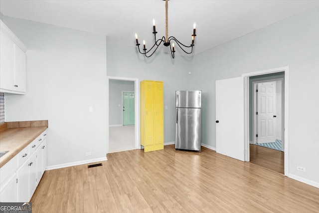 unfurnished dining area featuring baseboards, light wood finished floors, visible vents, and an inviting chandelier