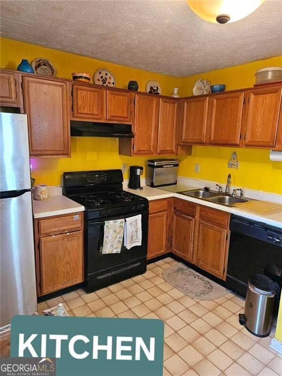 kitchen with a sink, black appliances, light countertops, under cabinet range hood, and a textured ceiling