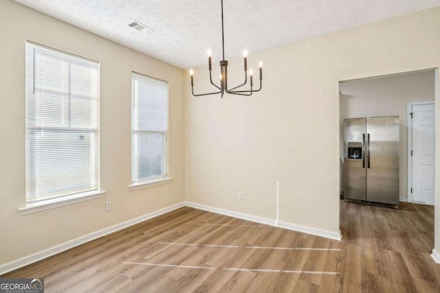 unfurnished dining area featuring a textured ceiling, baseboards, a chandelier, and wood finished floors