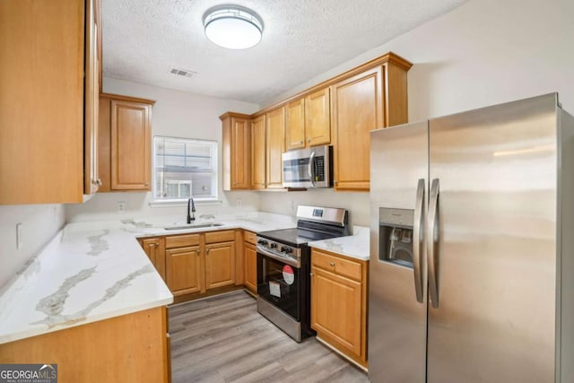 kitchen featuring light wood finished floors, visible vents, appliances with stainless steel finishes, a textured ceiling, and a sink