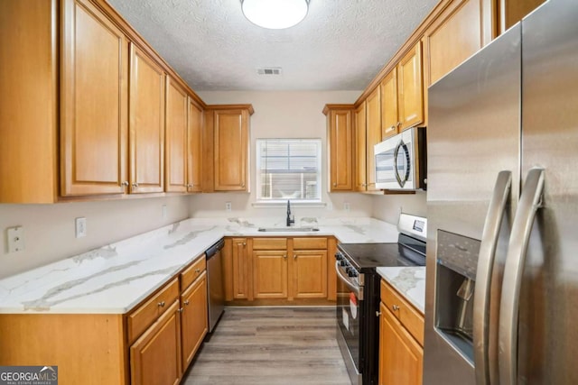 kitchen featuring a textured ceiling, a sink, light wood-style floors, appliances with stainless steel finishes, and light stone countertops