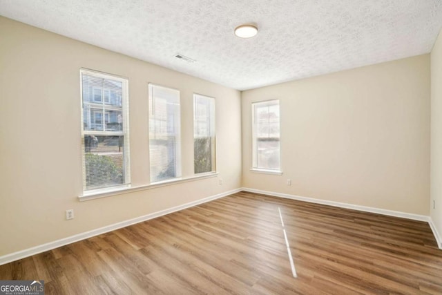 spare room featuring visible vents, a textured ceiling, baseboards, and wood finished floors