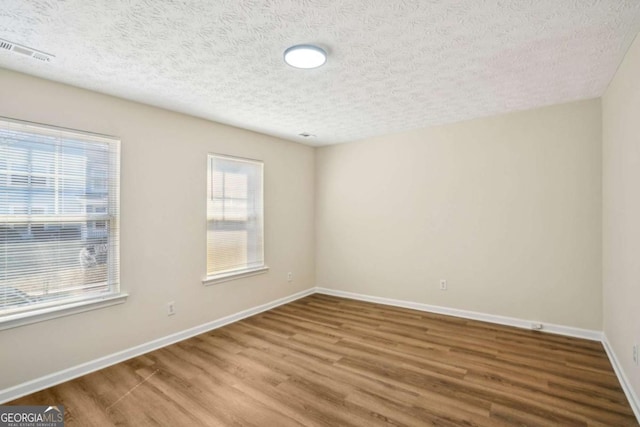 spare room featuring baseboards, a textured ceiling, visible vents, and wood finished floors