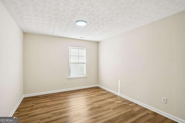 spare room with a textured ceiling, baseboards, and wood finished floors