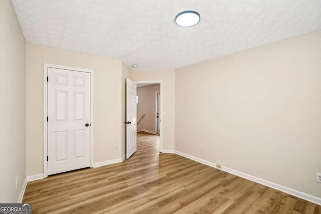 unfurnished bedroom with light wood-type flooring, a textured ceiling, and baseboards