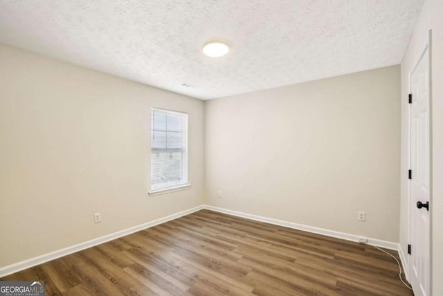 unfurnished bedroom with a textured ceiling, wood finished floors, and baseboards