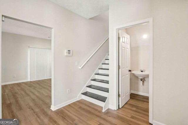 staircase with a textured ceiling, baseboards, and wood finished floors