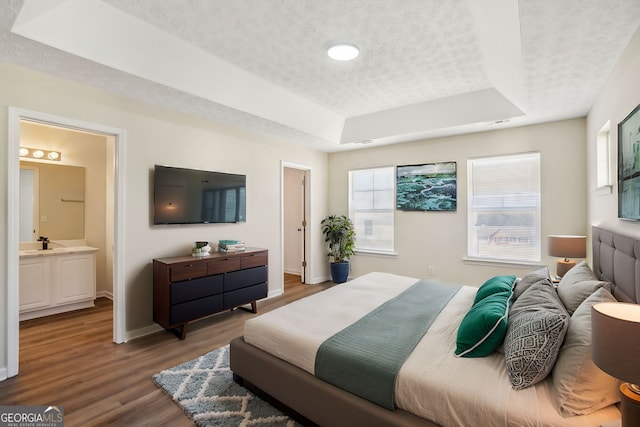 bedroom with a textured ceiling, a sink, wood finished floors, baseboards, and a tray ceiling