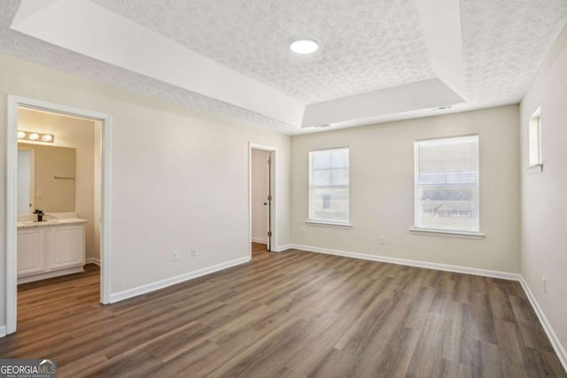 unfurnished bedroom with dark wood-type flooring, a tray ceiling, a textured ceiling, and baseboards