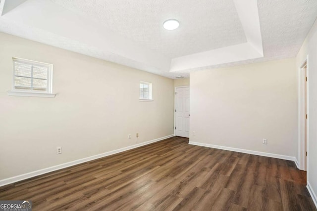 interior space with a tray ceiling, dark wood-style flooring, a textured ceiling, and baseboards