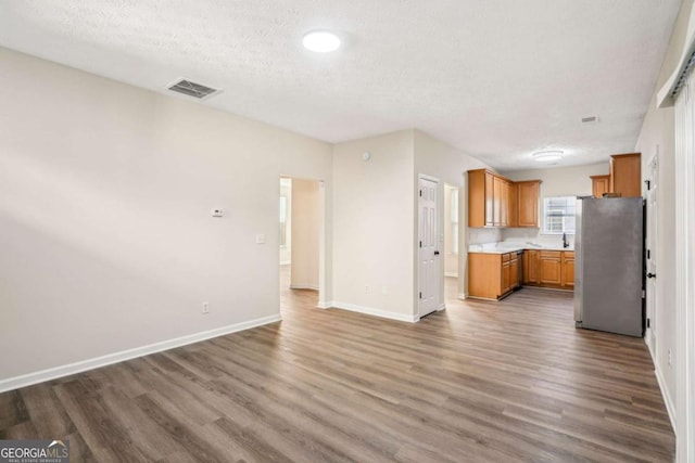 kitchen featuring visible vents, brown cabinetry, wood finished floors, freestanding refrigerator, and light countertops