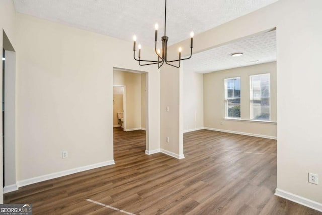 unfurnished dining area featuring an inviting chandelier, a textured ceiling, baseboards, and wood finished floors