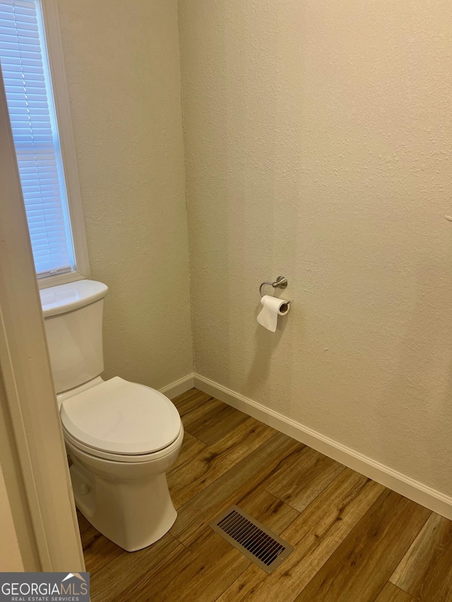 bathroom featuring visible vents, a textured wall, toilet, wood finished floors, and baseboards