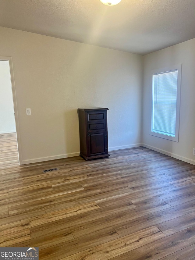 interior space with visible vents, a textured ceiling, baseboards, and wood finished floors