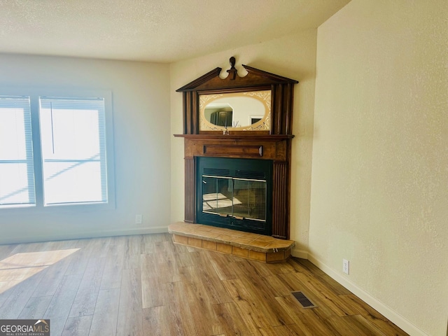 unfurnished living room with baseboards, visible vents, wood finished floors, a textured ceiling, and a fireplace