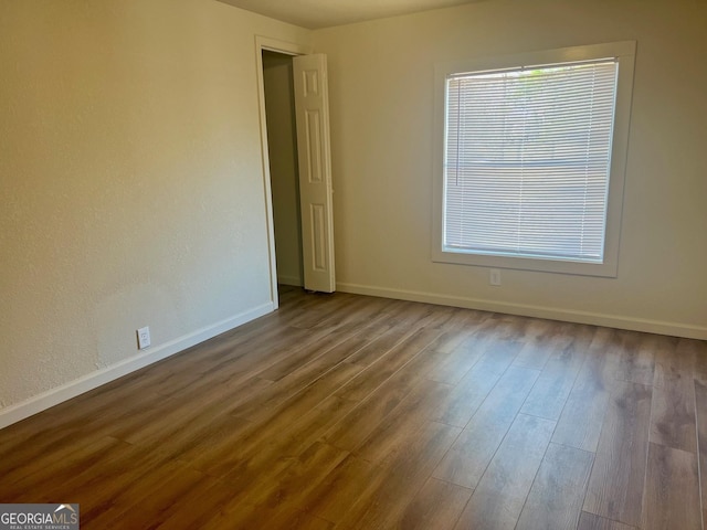 empty room with a healthy amount of sunlight, wood finished floors, and baseboards