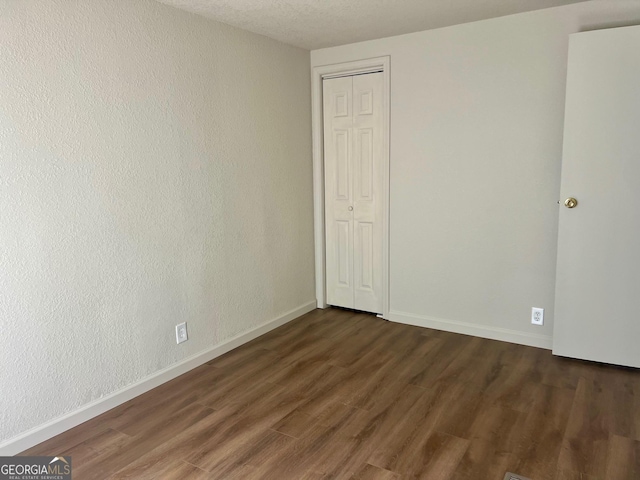 unfurnished bedroom featuring a closet, baseboards, dark wood-style flooring, and a textured wall