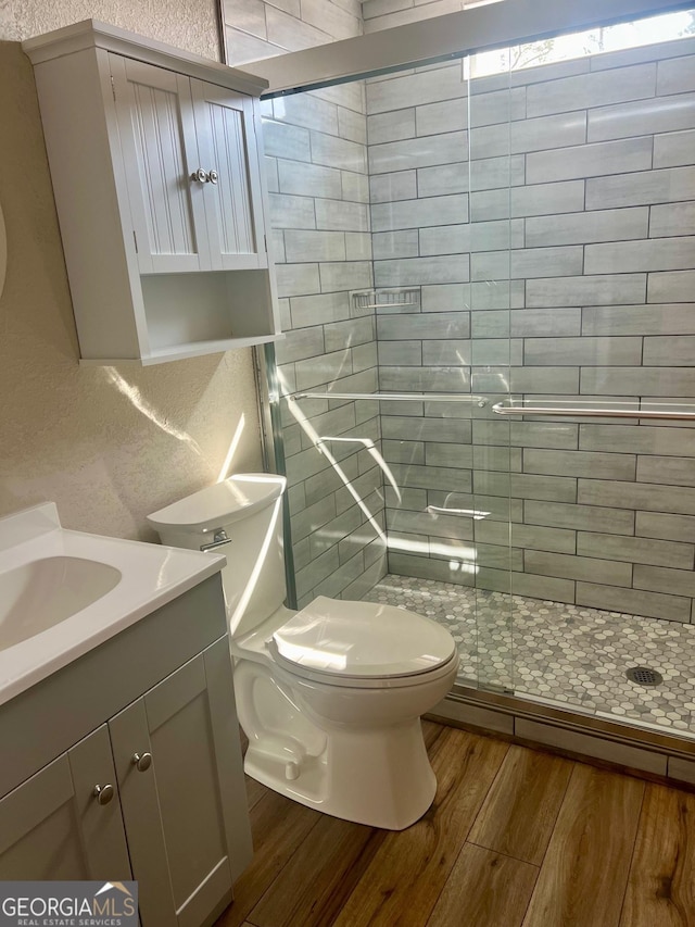 full bathroom featuring a stall shower, a textured wall, toilet, wood finished floors, and vanity