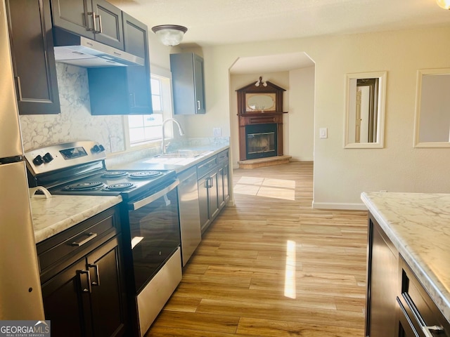 kitchen with electric stove, backsplash, light wood-type flooring, under cabinet range hood, and a sink