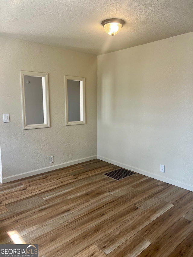 unfurnished room with visible vents, a textured ceiling, baseboards, and wood finished floors