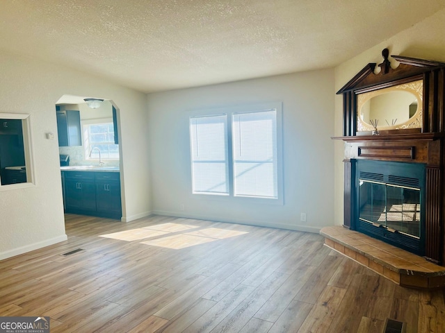 unfurnished living room with light wood-style flooring, visible vents, a textured ceiling, and a glass covered fireplace