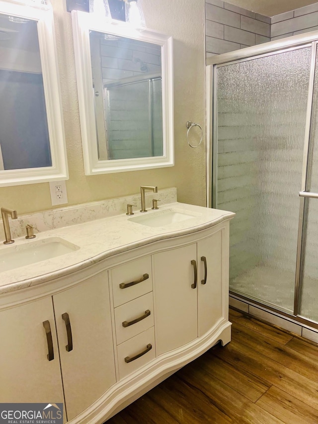 full bathroom featuring double vanity, wood finished floors, a sink, and a shower stall