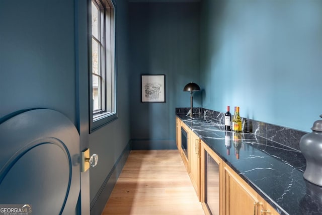 bar featuring beverage cooler, indoor wet bar, light wood-style flooring, and baseboards