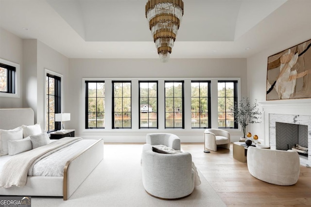 bedroom with a fireplace, a raised ceiling, wood finished floors, and multiple windows