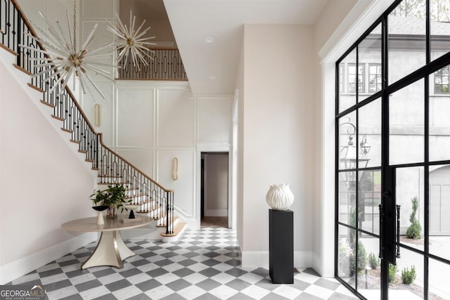 entrance foyer featuring an inviting chandelier, a decorative wall, baseboards, and stairs