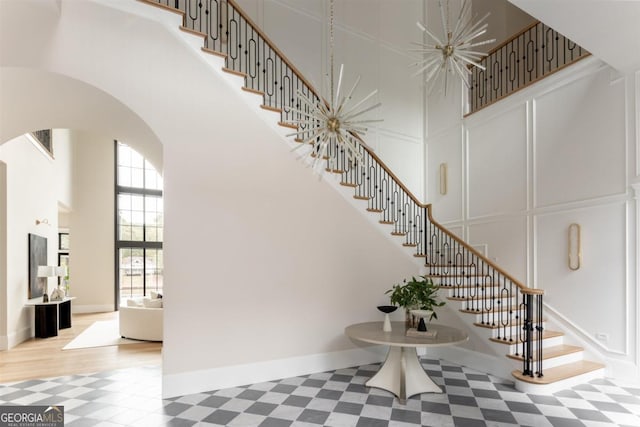 stairway with a towering ceiling, arched walkways, a decorative wall, and tile patterned floors